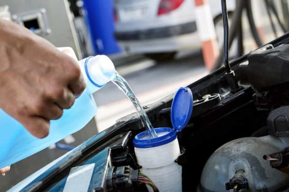 pouring blue washer fluid into the intake under the car hood